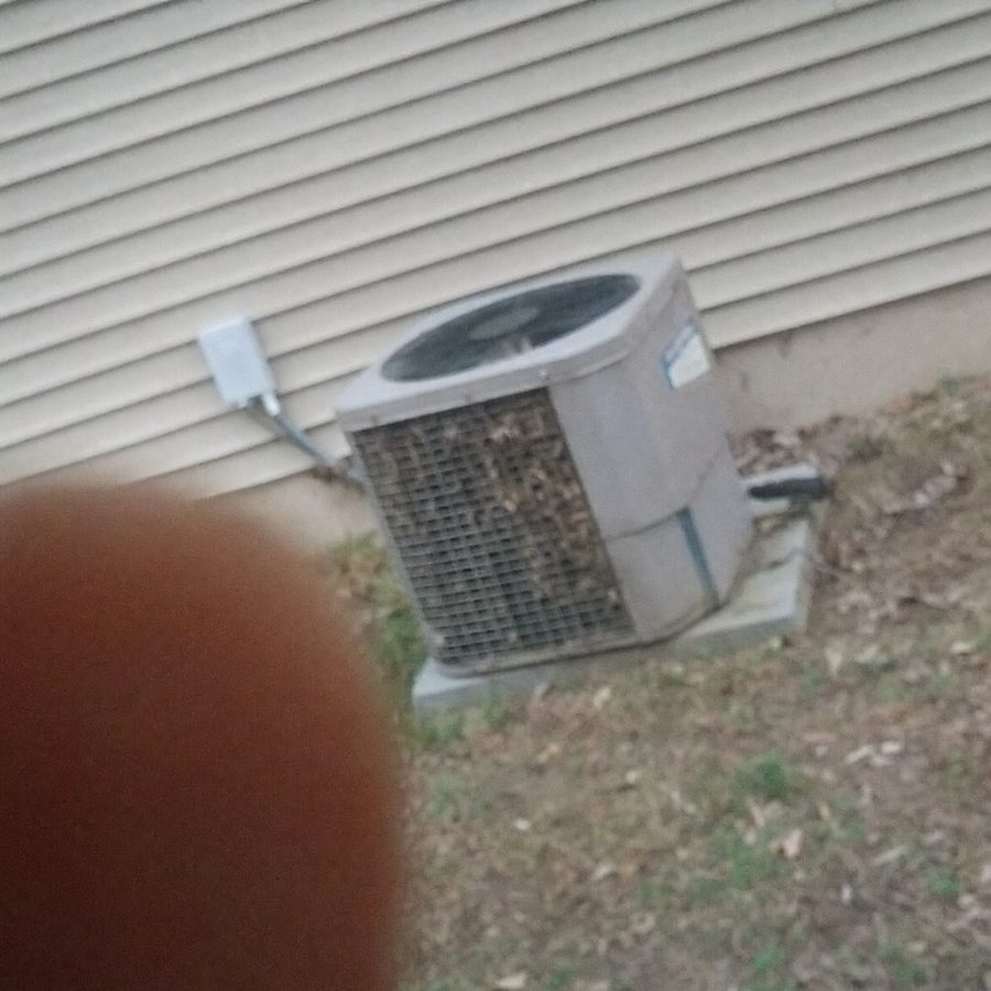 Phone photo of an outdoor AC condenser beside a house, debris in its fins
