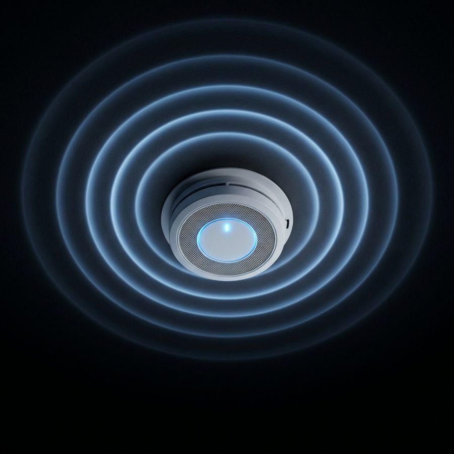 A round alarm on a dark ceiling with its indicator light on