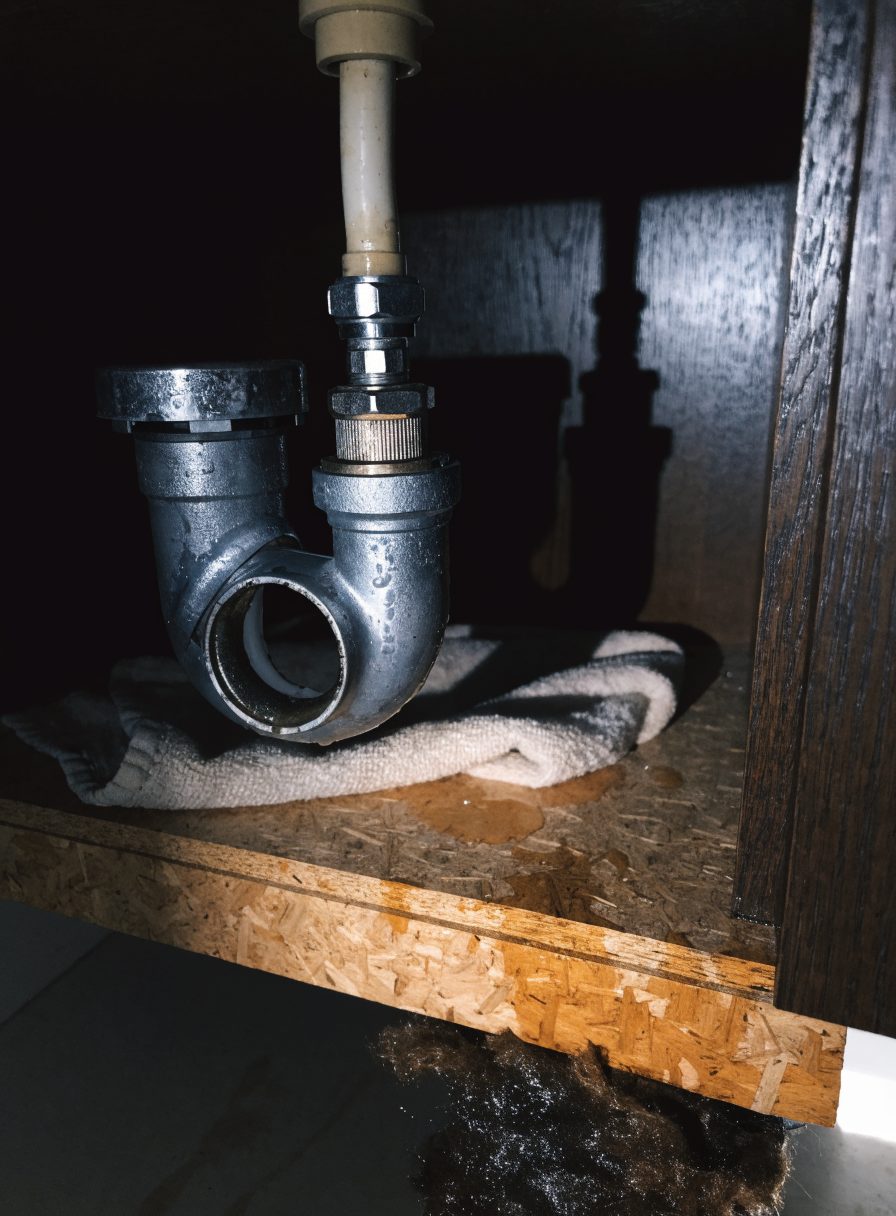 A dripping pipe under a kitchen sink, a towel underneath
