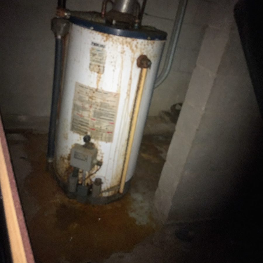 A rusty water heater in a dim basement closet