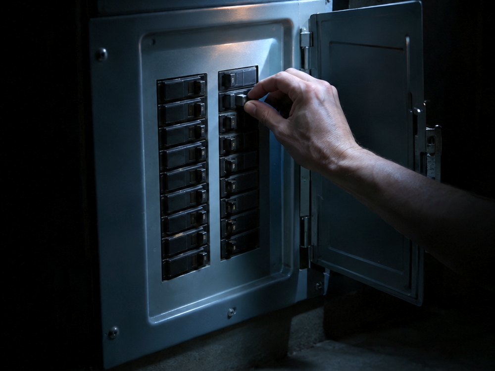 A hand on a breaker in an open panel