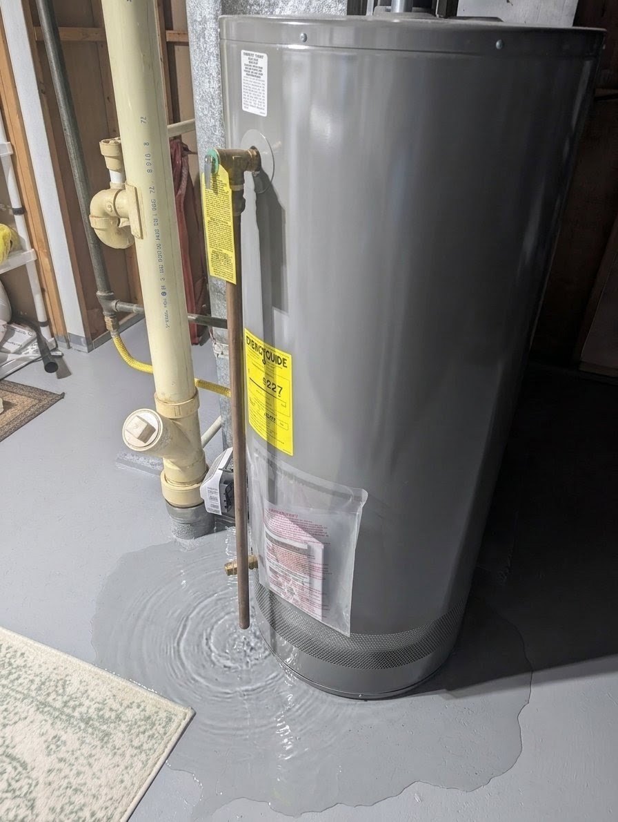 A gas water heater in a basement with a wide puddle of water spreading from its base