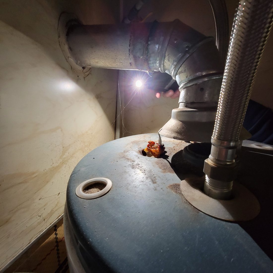 The top of a gas water heater: rust and debris around the flue connection and the water lines