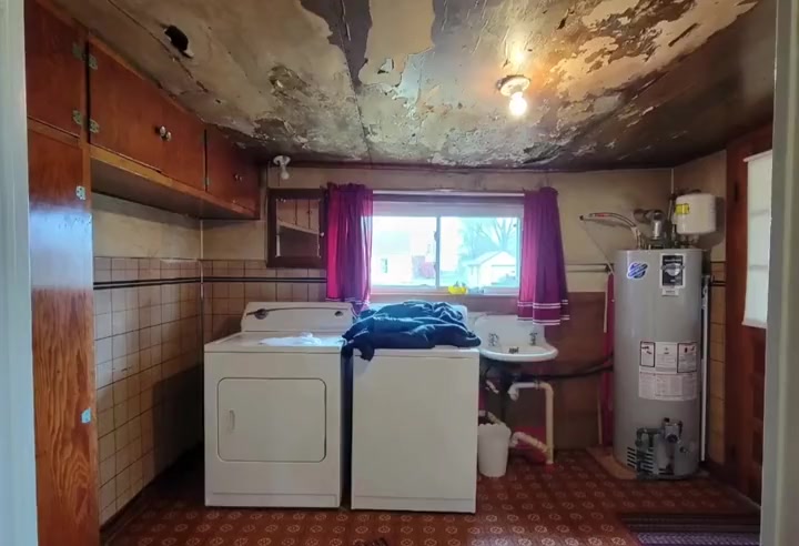 The laundry room before: peeling ceiling, old cabinets, washer, dryer and water heater