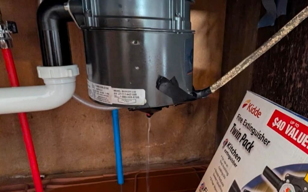A garbage disposal under a kitchen sink, leaking onto the cabinet floor — photographed in a building we own